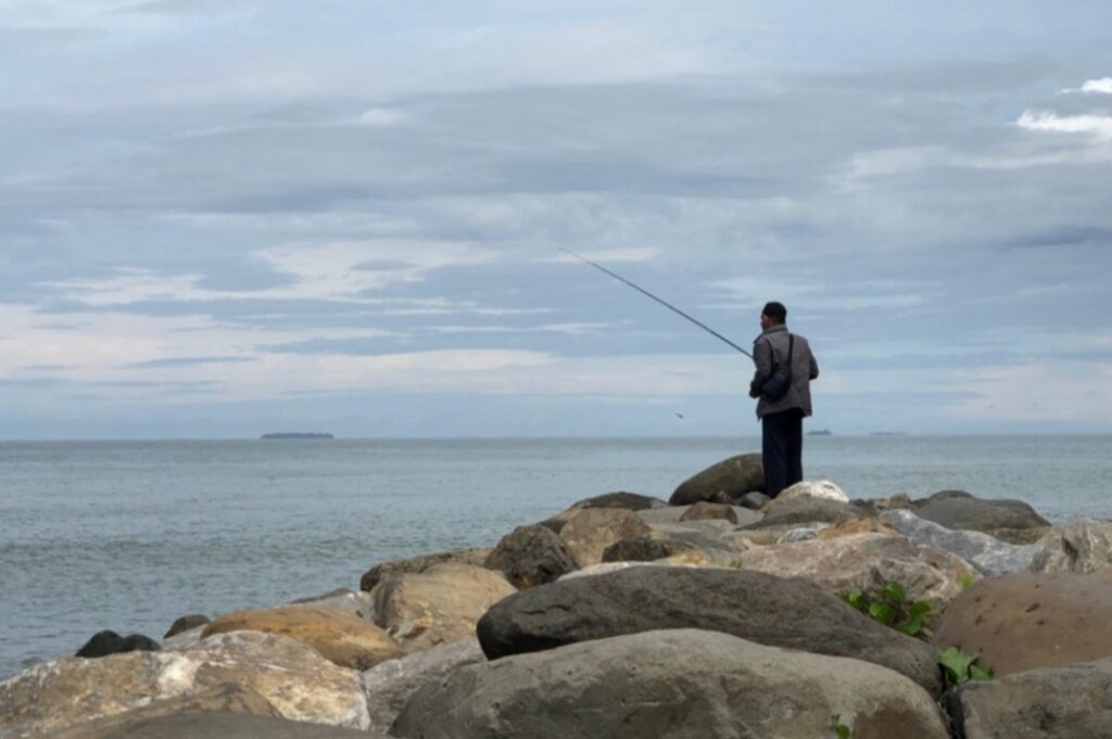 Seorang warga Padang tengah memancing di atas breakwater seawall. Batu pemecah gelombang ini akan diperkuat oleh Pemerintah Kota Padang. HALUAN.