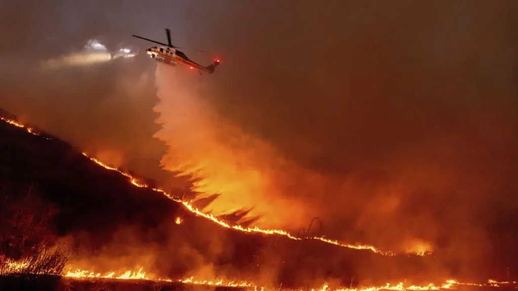 Helikopter pemadam dikerahkan untuk menanggulangi kebakaran yang semakin meluas di kawasan West Hills, Los Angeles, yang semakin cepat menyebar akibat hembusan angin yang sangat kuat. (Foto: Associated Press)